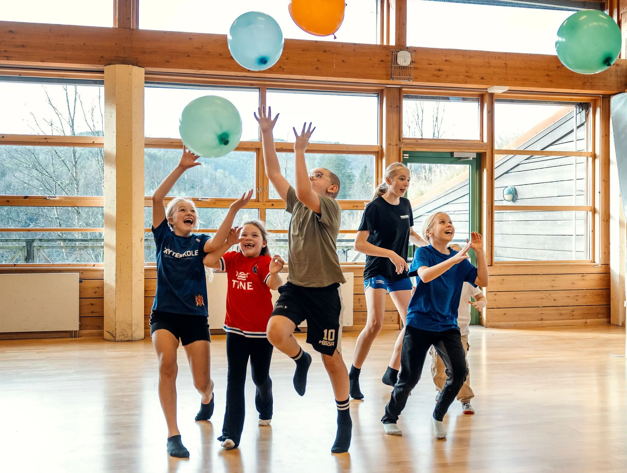 Barn og ungdom i gymsal med ballonger. Foto.