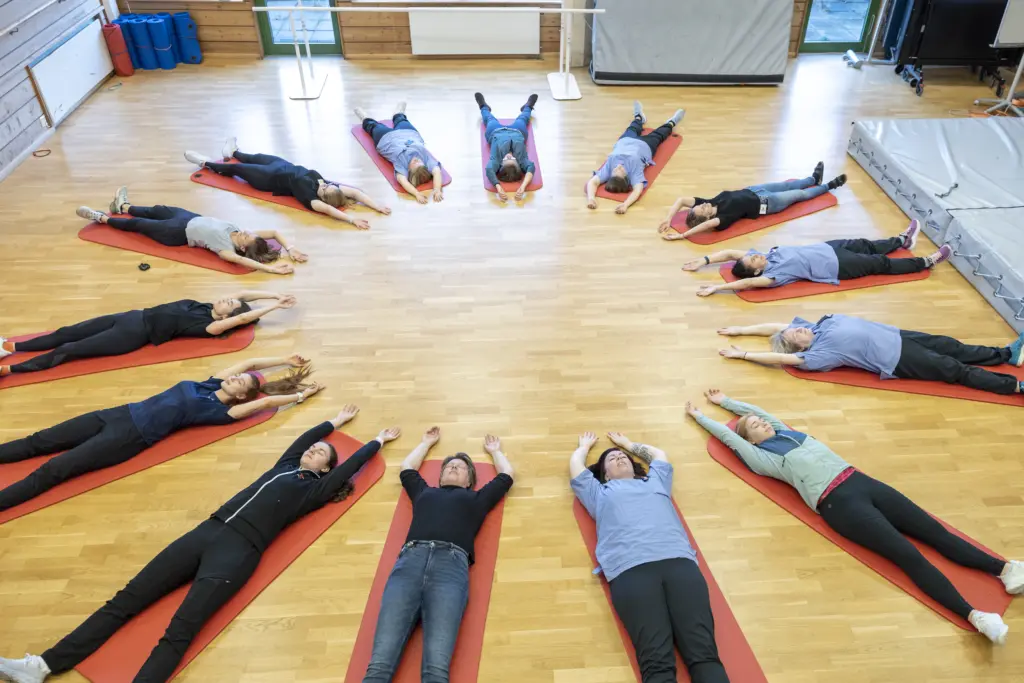 Folk ligger på matter i ring i gymsal. Foto. 