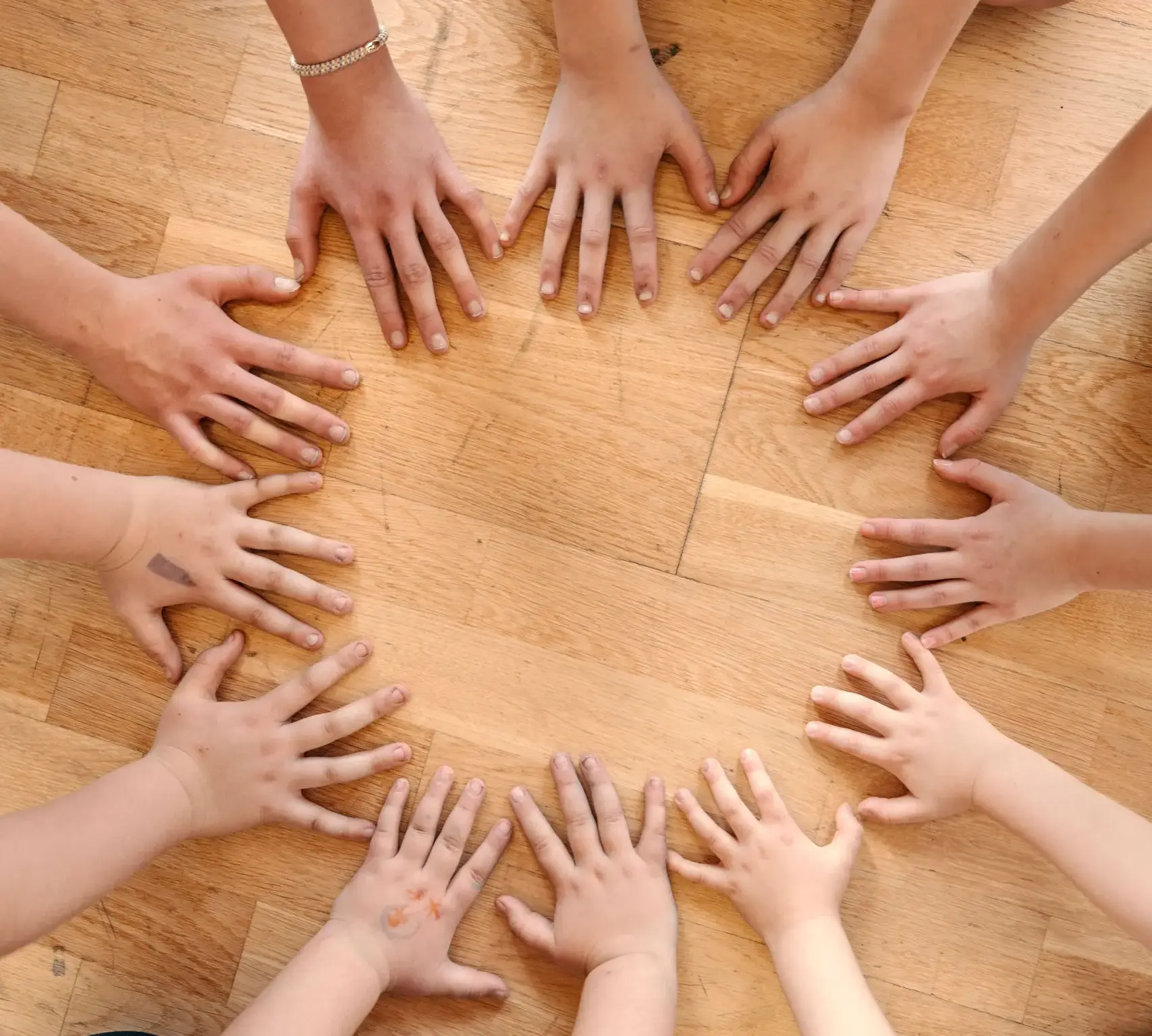 Mange hender i sirkel mot et golv. Foto.